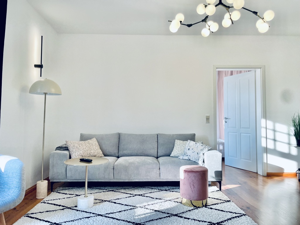 Wohnbereich der Suite – graues Sofa, rosa Pouf, Stehlampe auf hellem Parkett